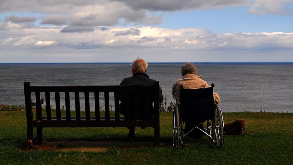 Äldre par sitter på parkbänk vid havet